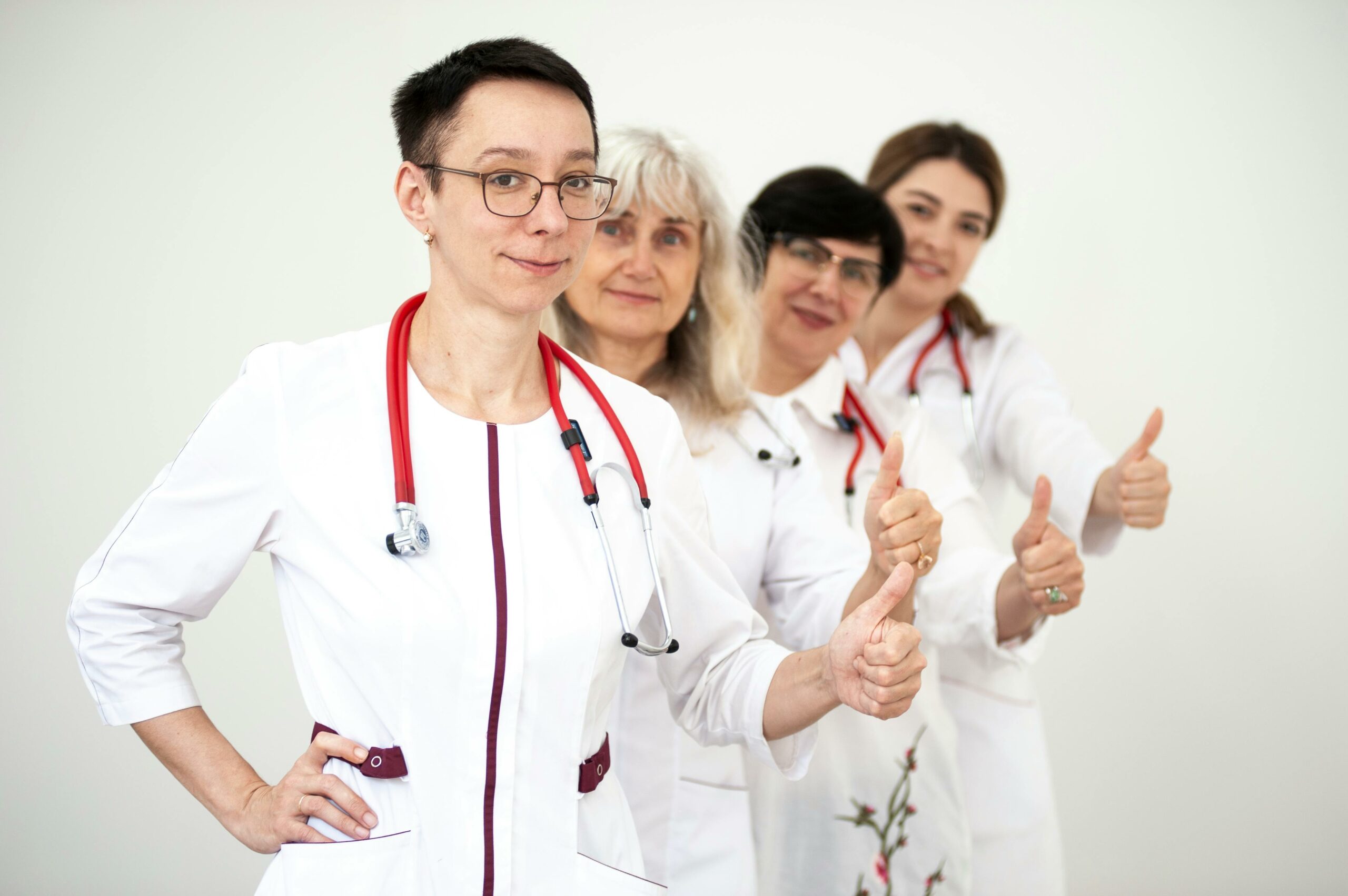 A group of female doctors in white coats showing thumbs up, symbolizing teamwork and women empowerment in healthcare.